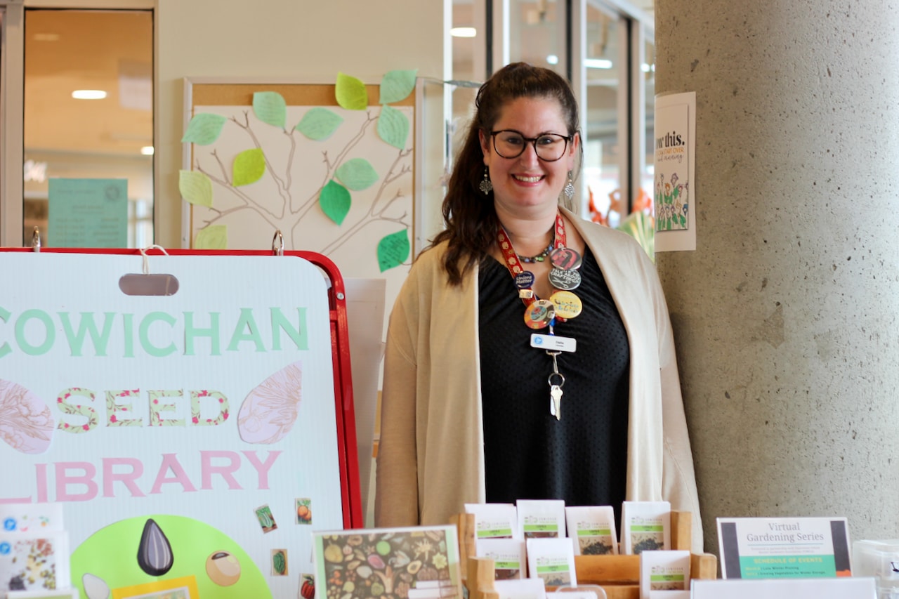 A woman smiles in front of a sign that reads, "Cowichan Seed Library."
