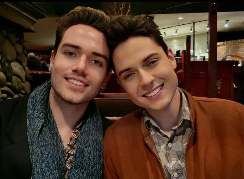 Frankie Bouchier and Joshua Holloway, two white men, rest heads against one another as they both look at the camera and smile.
