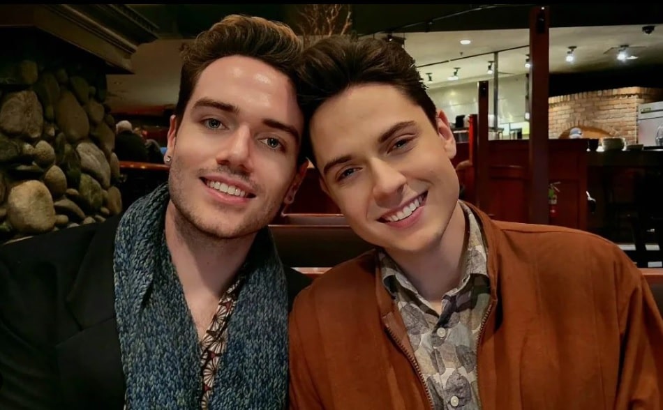 Frankie Bouchier and Joshua Holloway, two white men, rest heads against one another as they both look at the camera and smile while celebrating the premier of their musical Distance.