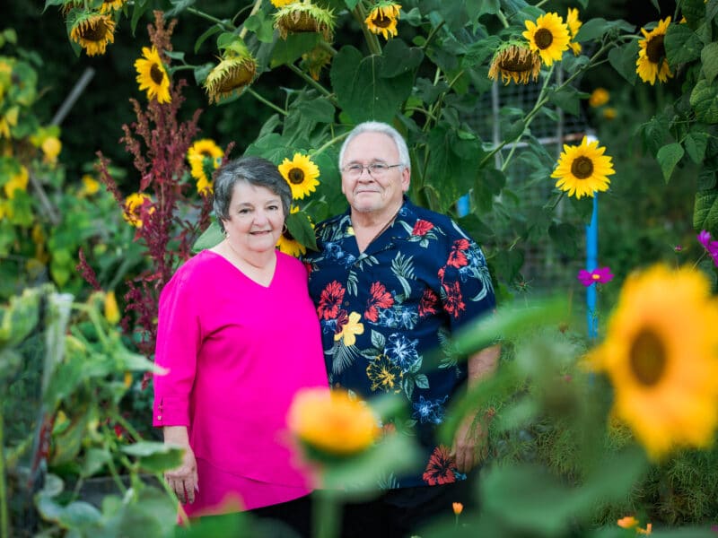 An older couple surrounded by sunflowers.