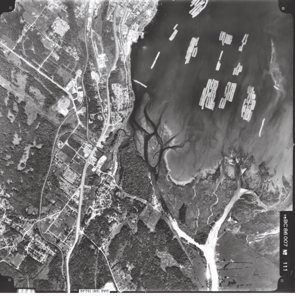 A black and white aerial image from 1986 shows historical developments of this ancient village site include logging, rail and mining.