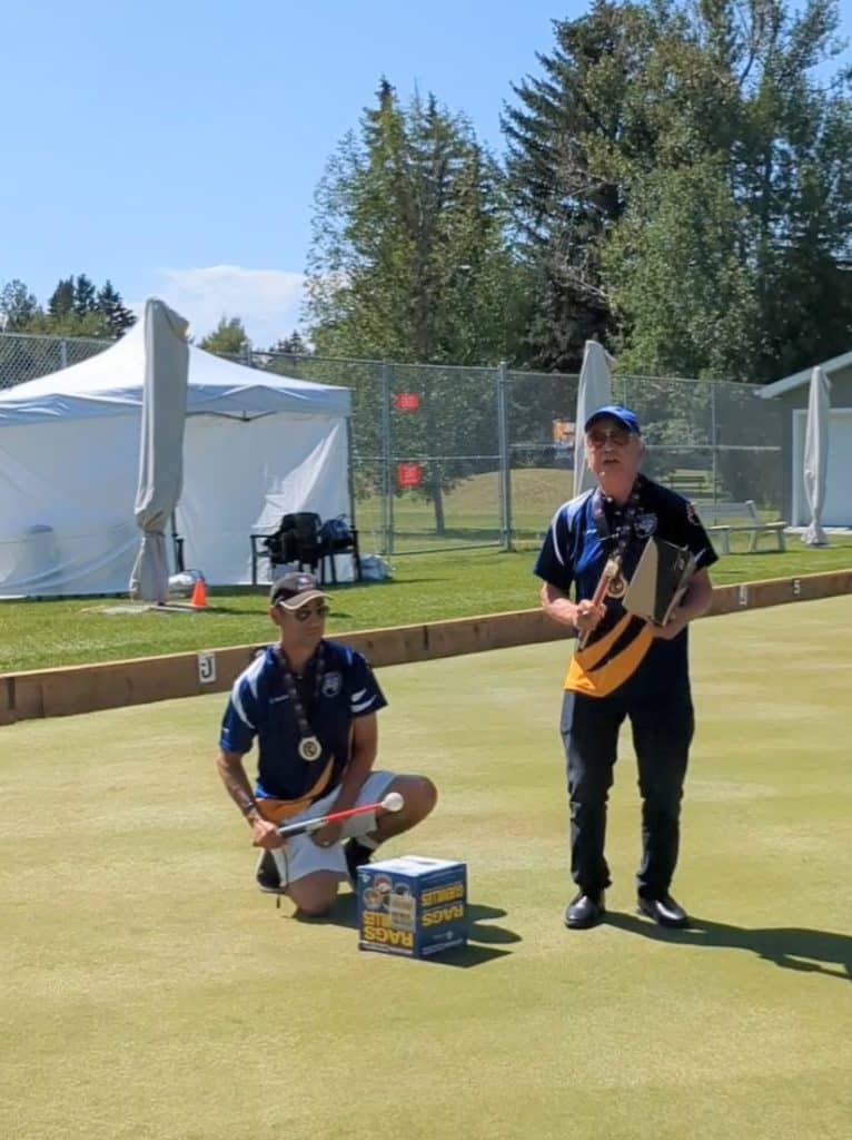 Two Indigenous drummers, Jay Gatley and Randy Fred, stand on the grass, sing and play makeshift drums on cardboard boxes.