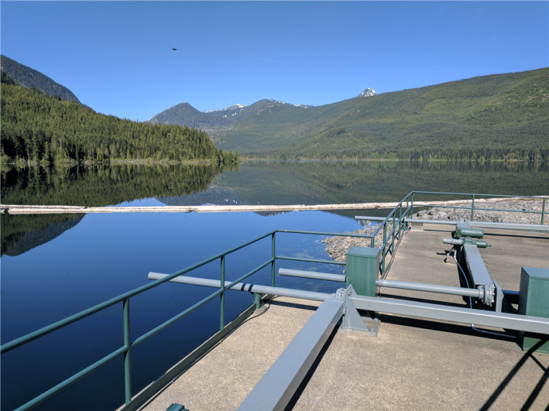 A full, dammed lake is shown with a railing access point and pipes.