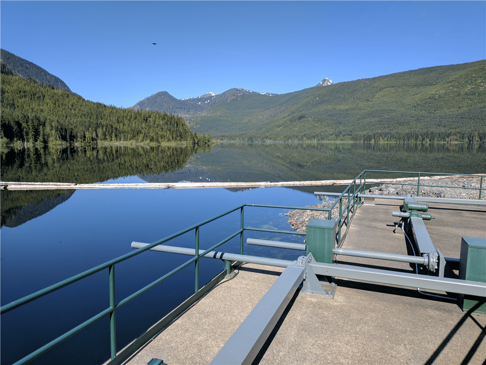 A full, dammed lake is shown with a railing access point and pipes.