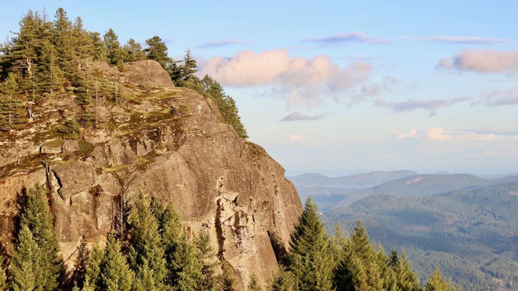 A rocky mountain top in  front of sky and distant land below