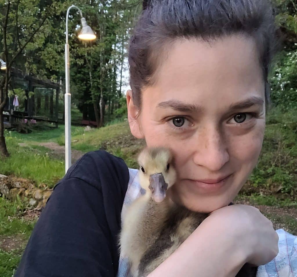 A woman with brown hair cuddles a baby goose