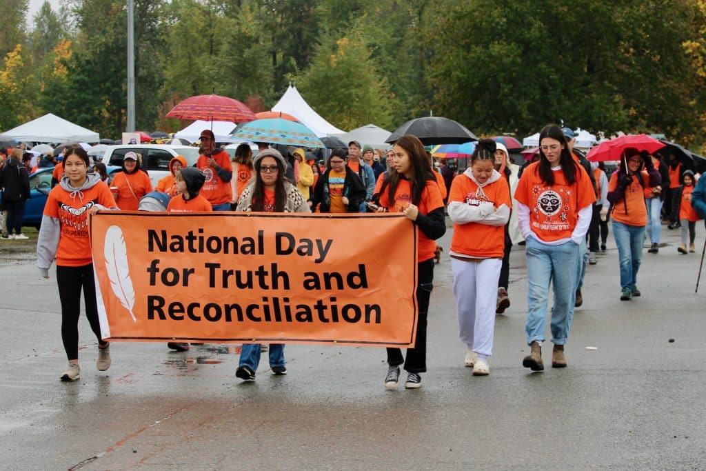 An orange banner reads "National Day for Truth and Reconciliation." Young people wearing orange walk while holding the banner.