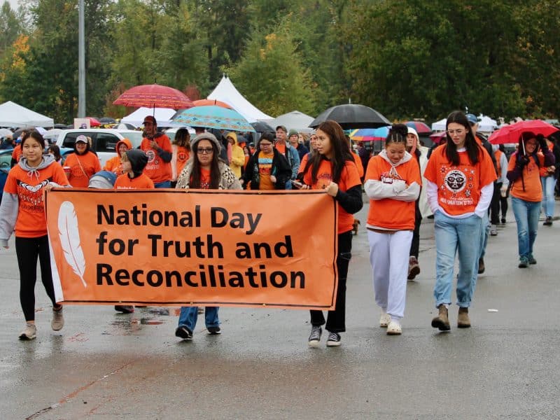 An orange banner reads "National Day for Truth and Reconciliation." Young people wearing orange walk while holding the banner.