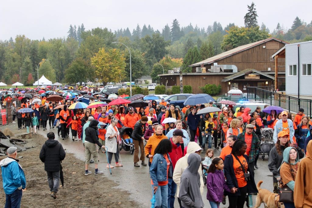 A very large crowd of people walking, many wearing orange and many carrying umbrellas.