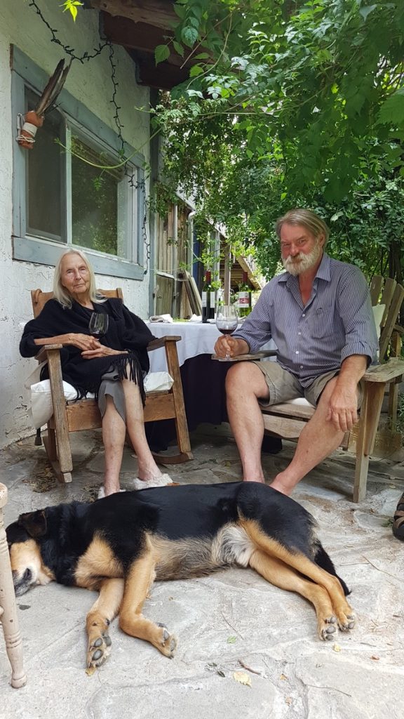 Bernice Woollam sits (left) in a chair next to Rowan Hamilton (right) outside on The Hawthorn property. A dog lies on the ground in front of them.