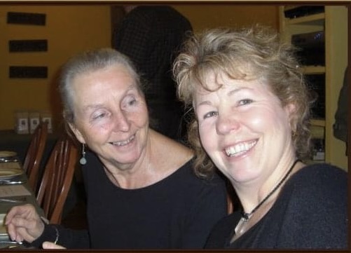 A photo of Bernice Woollam and Kelly Johnson, sitting side-by-side, smiling. Woollam is looking at Johnson (right) and Johnson is looking at the camera.