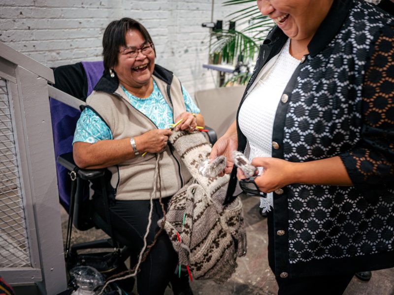 Two women laugh while knitting a Cowichan Sweater