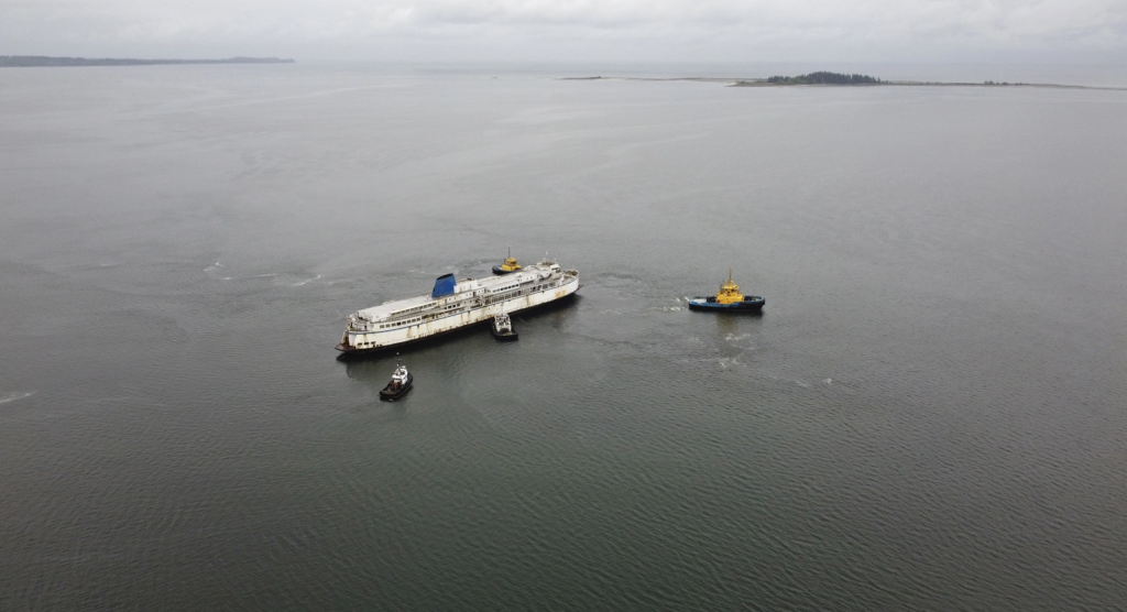tugboats pull an old ferry vessel