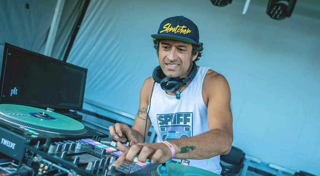 DJ Peter Poole twiddles knobs on a turntable mixer wearing a black ball cap with yellow writing