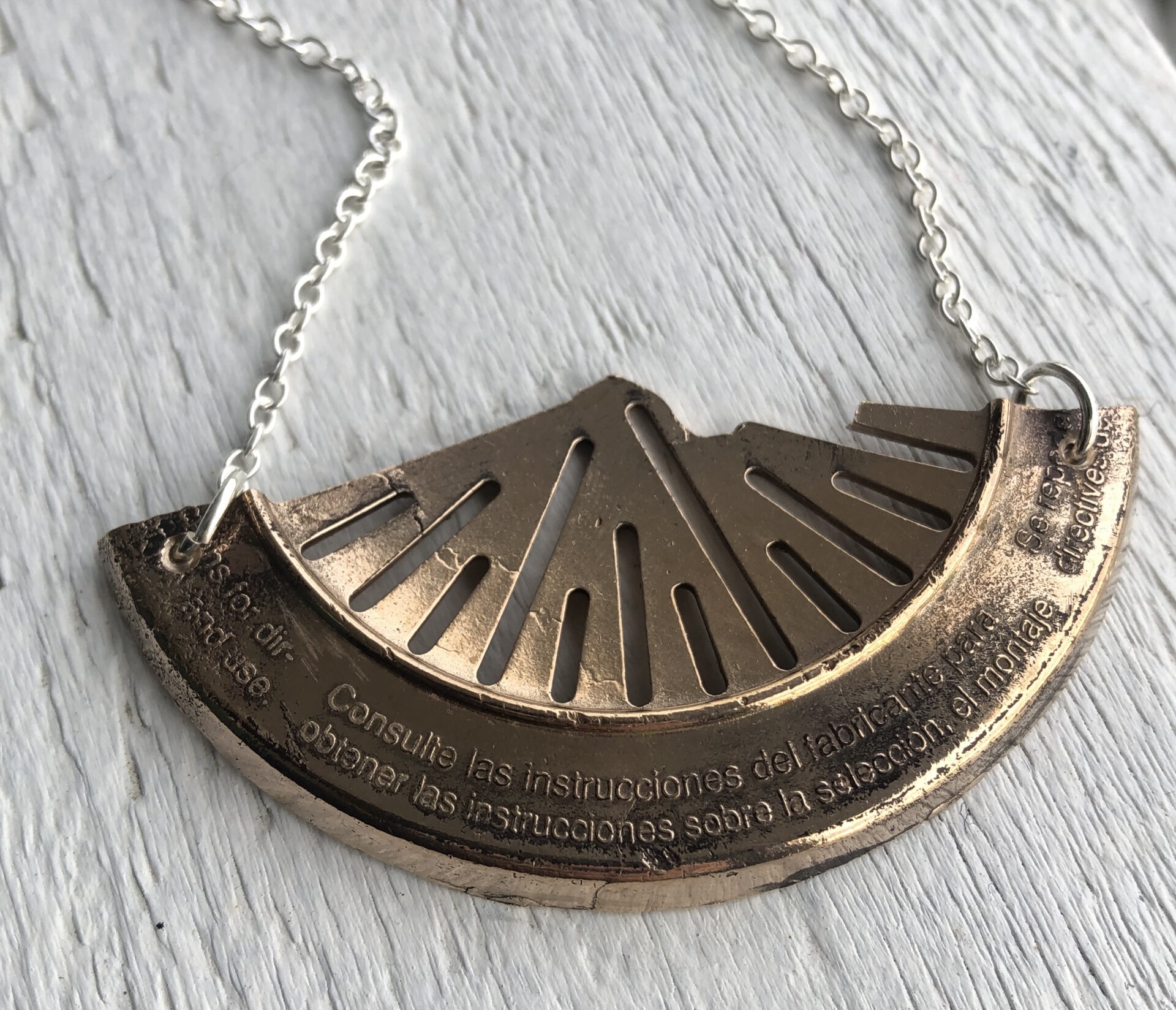 A bronze necklace cast from a broken piece of plastic with writing on the edge and slits hangs on a silver chain