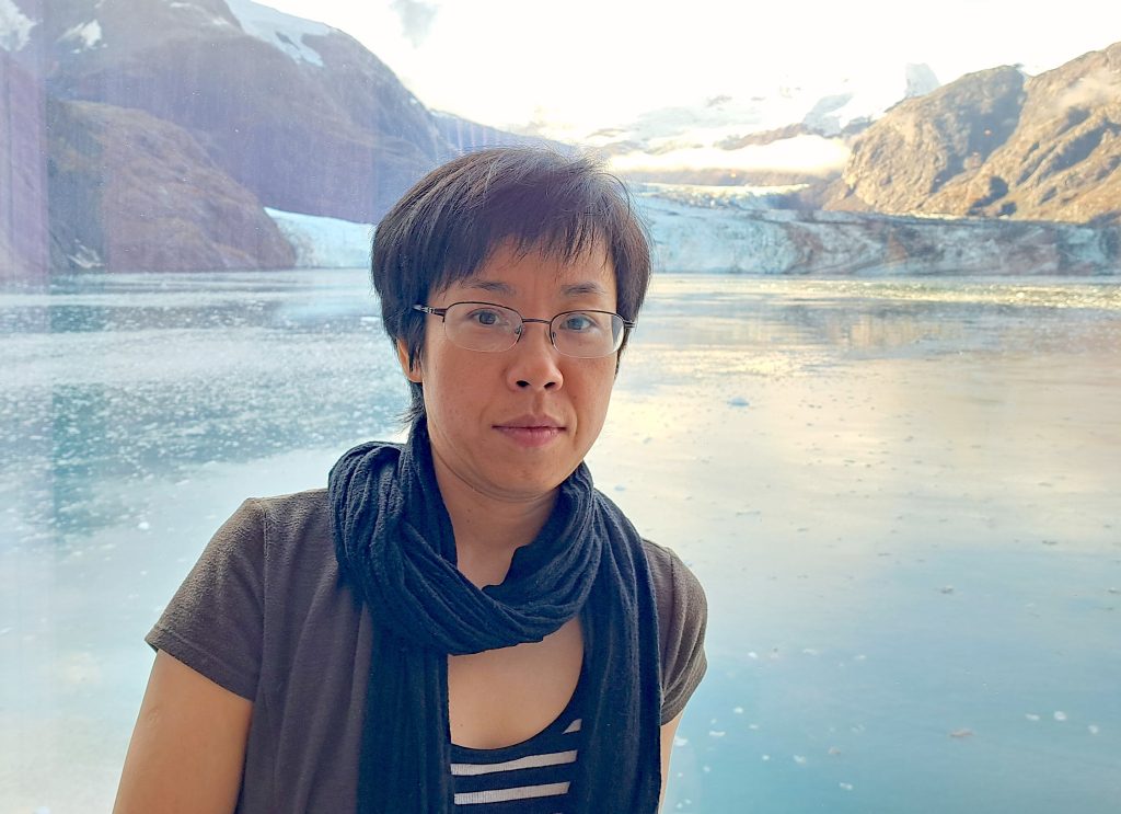 a woman with short hair and glasses stands in front of an ocean scene