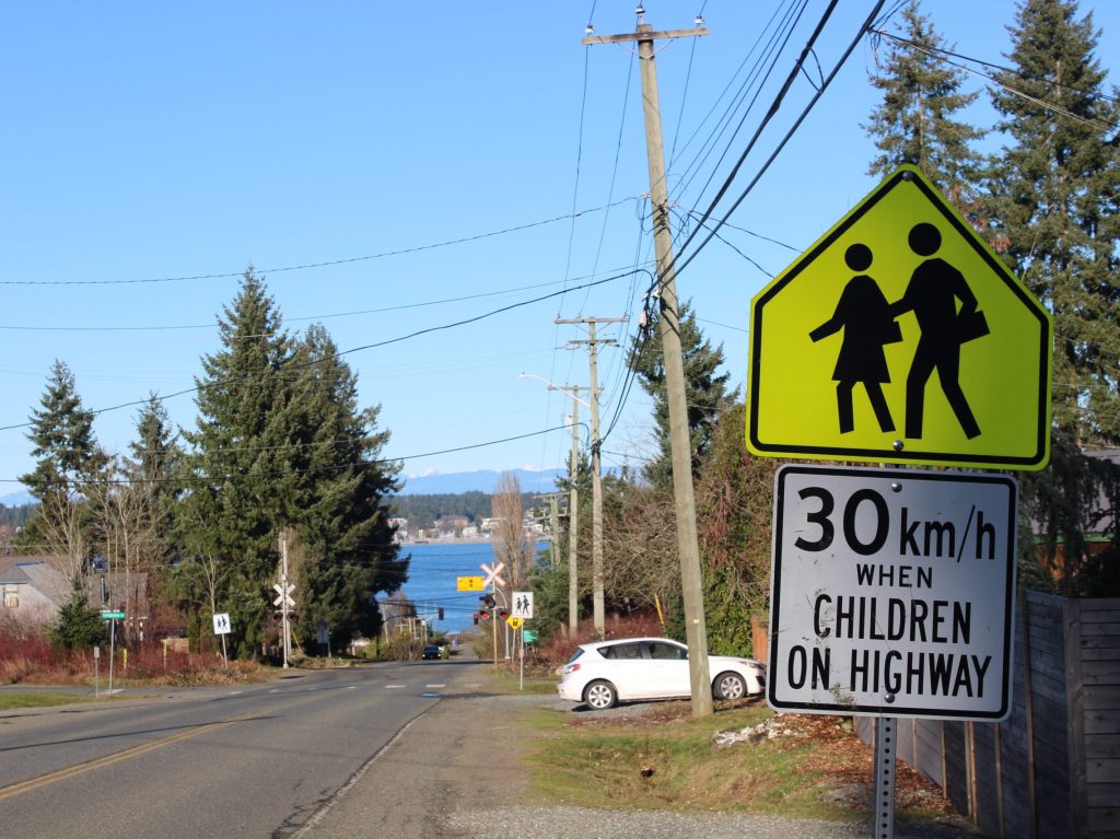A road with a sign on the right that advises caution around pedestrians and a 30 km/hr speed limit when children are on the road.