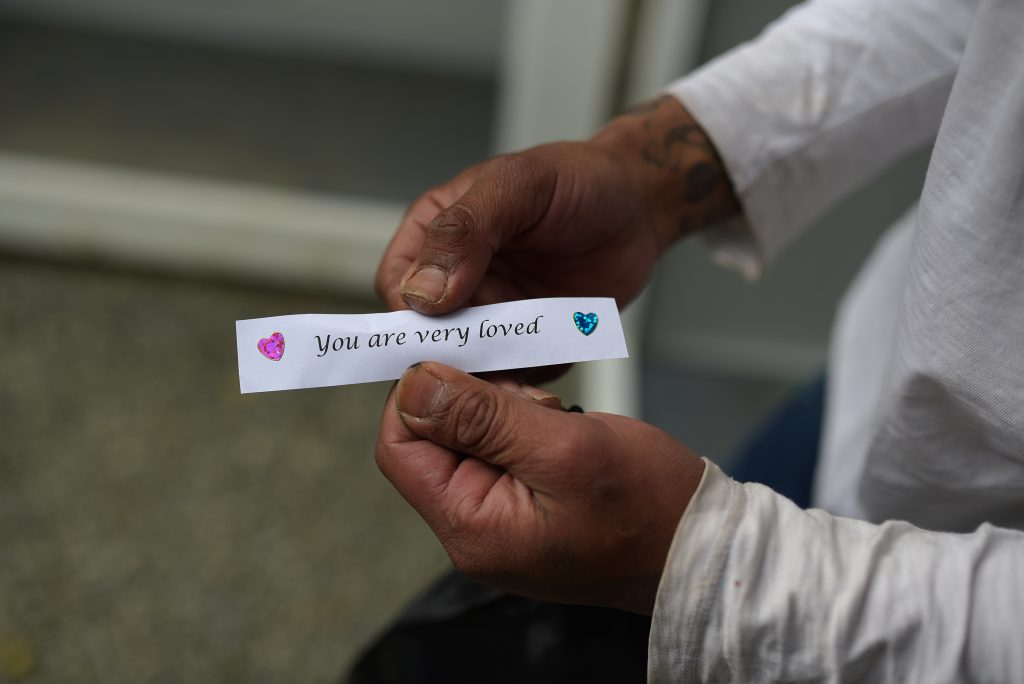 Hands hold a strip of paper that says "You are very loved" on it, with heart stickers on either side of the phrase.