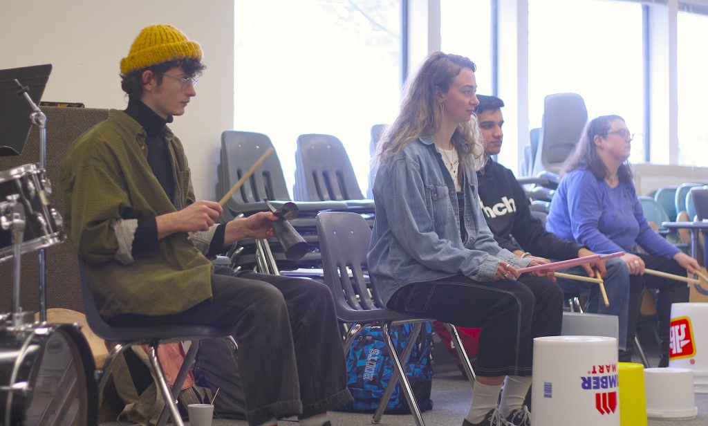 A group of students practice drumming on plastic tubs