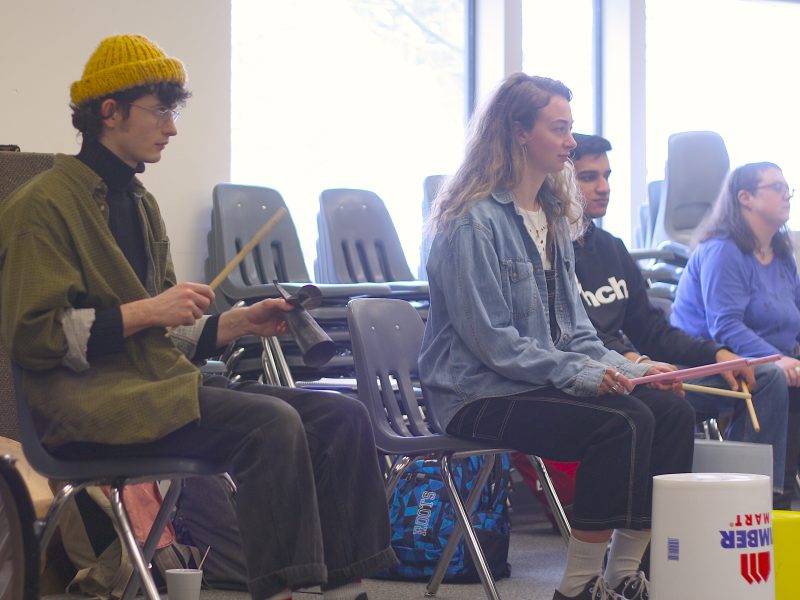 A group of students practice drumming on plastic tubs