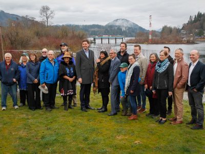 About 20 people pose for a group photo, with a lake and weir infrastructure in the background