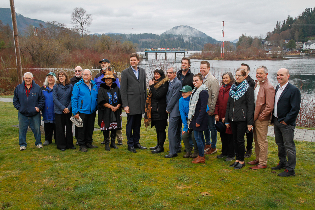 About 20 people pose for a group photo, with a lake and weir infrastructure in the background