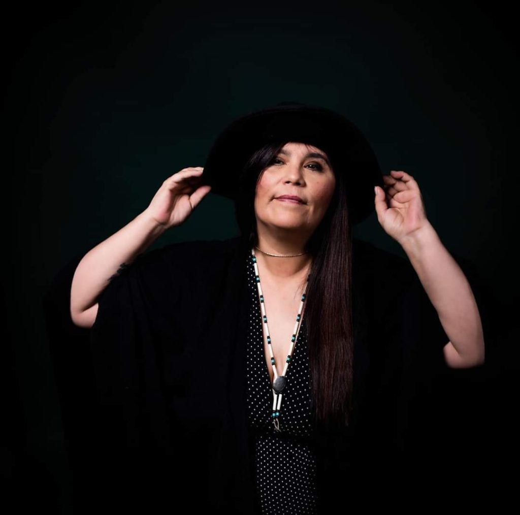 A woman in black raises her hands against a black background.
