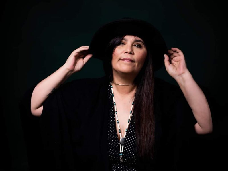 A woman in black raises her hands against a black background.