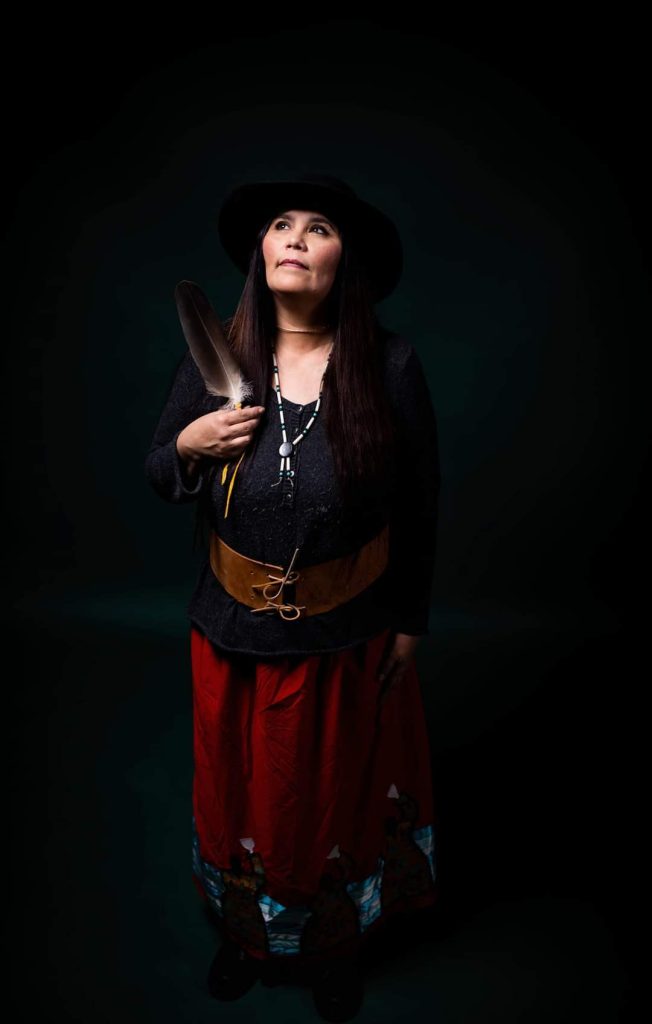 A woman holds an eagle feather and looks up pensively.