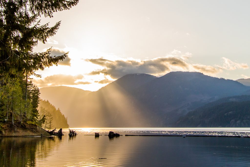 Sun peeks through the mountains and cloudsover Comox Lake