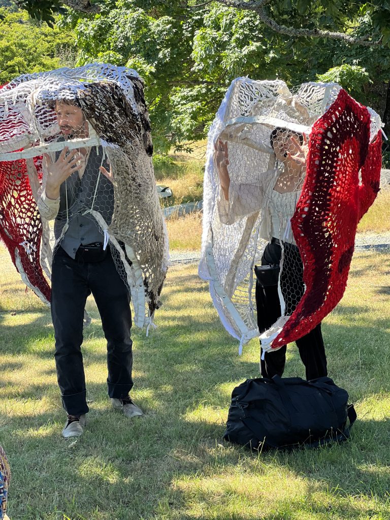 Two people stand inside what look like woven jellyfish shapes in a park