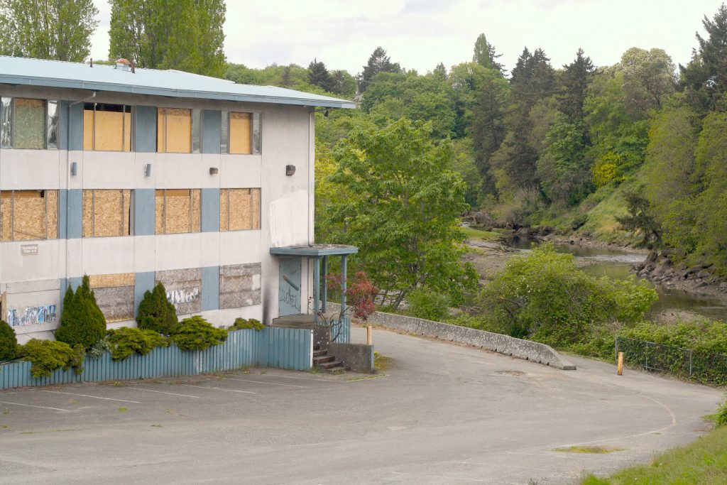 A shuttered and abandoned building sits at left and just beyond, the banks of the Millstone River, flanked by trees, is visible