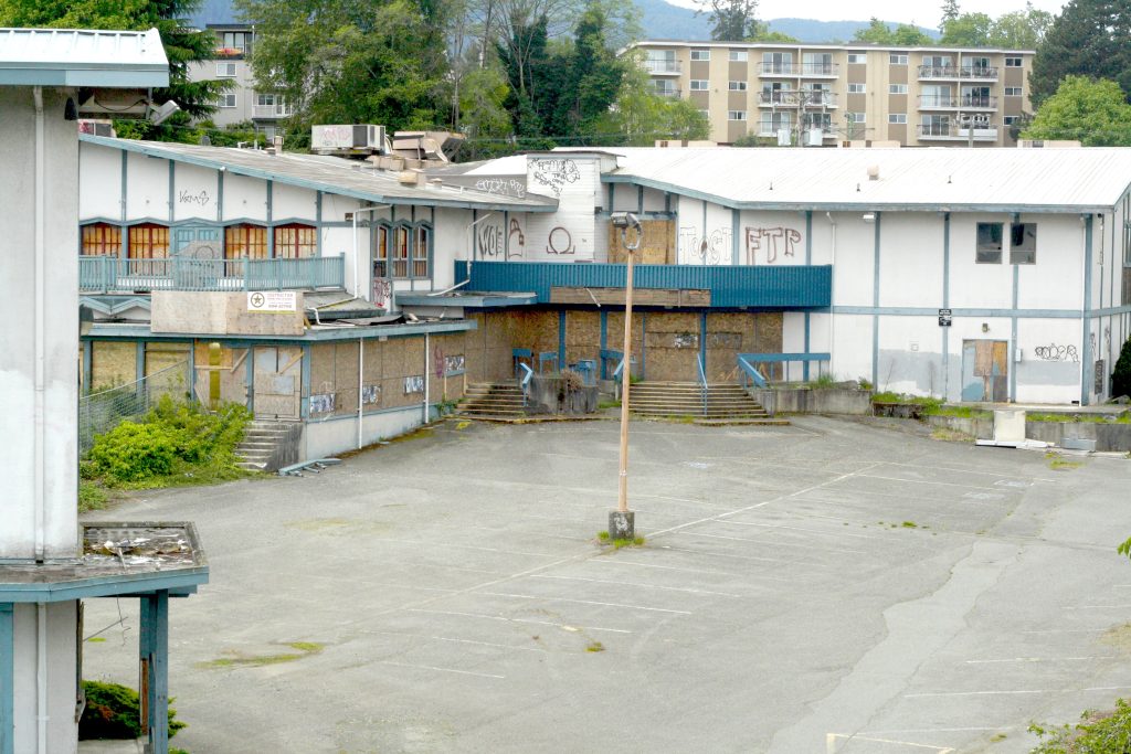 A boarded-up cluster of buildings covered in graffiti stands behind an empty parking lot.