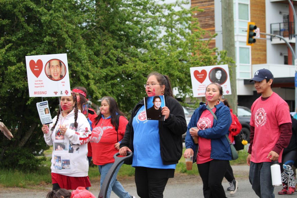 People march, wearing red and blue, holding photos and signs of missing and murdered loved ones.