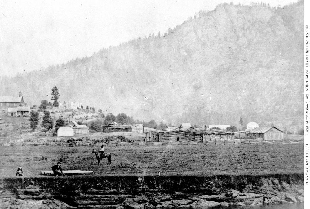 A black and white photo shows a log cabin in the background and a man on a horse. It depicts Comiaken Hill in Cowichan.