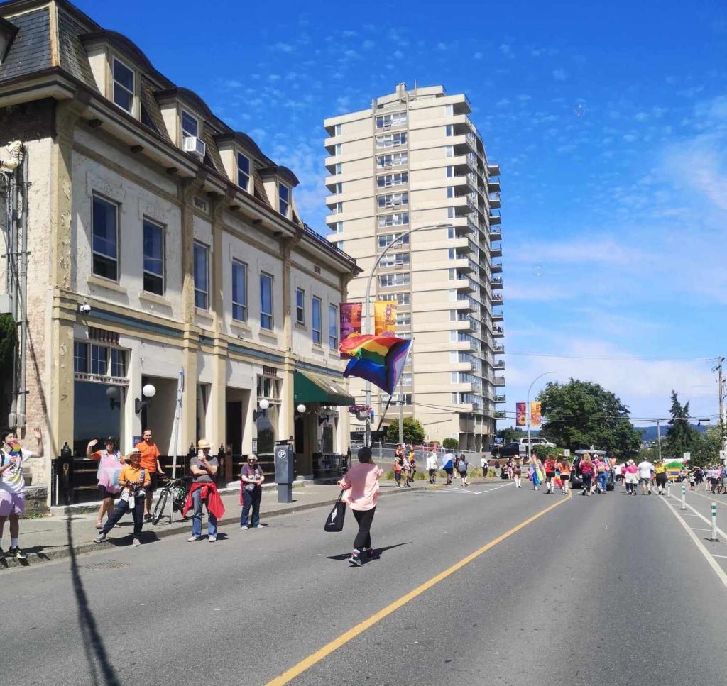 A person walks holding a large Pride flag down a street in Nanaimo.