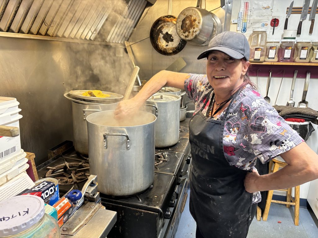 Cook, Deb Spaeth stirs food in a large metal pot in the kitchen of the Basket Society