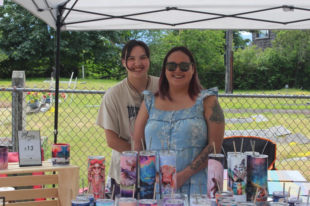 Two women stand behind their booth displaying a variety of thermoses decorated with different colourful designs.