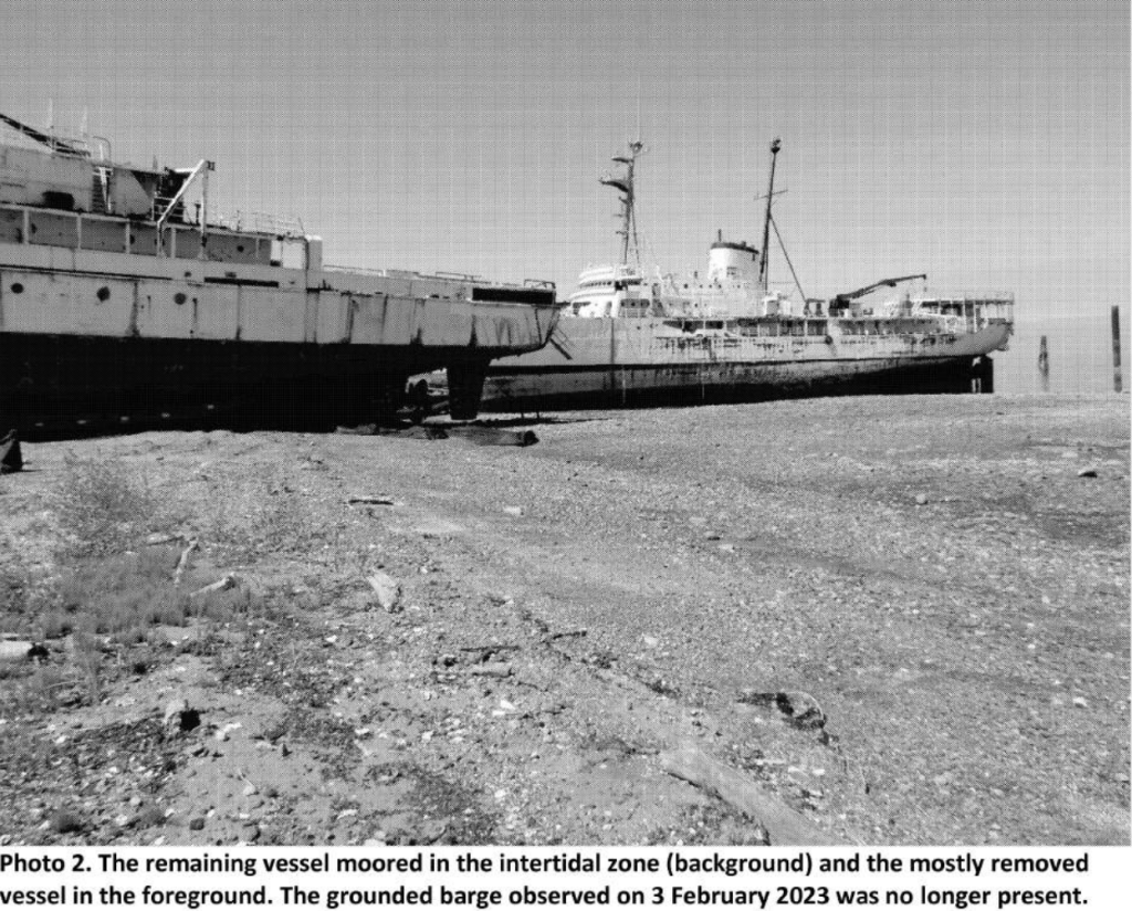 Black and white photo of two old vessels, one is in the intertidal zone and the other is on the beach. 