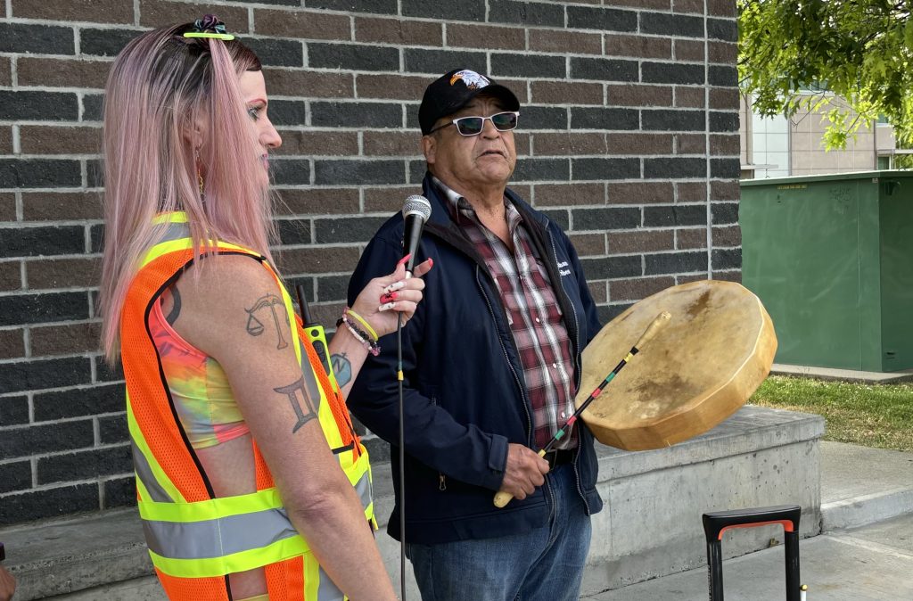 Drag performer Jerriana holds a microphone for Quw'utsun Elder Merle Seymour as he sings and drums.