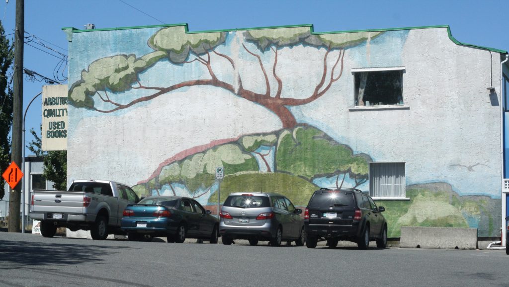 A mural featuring a stylized arbutus tree has cars parked in front of it