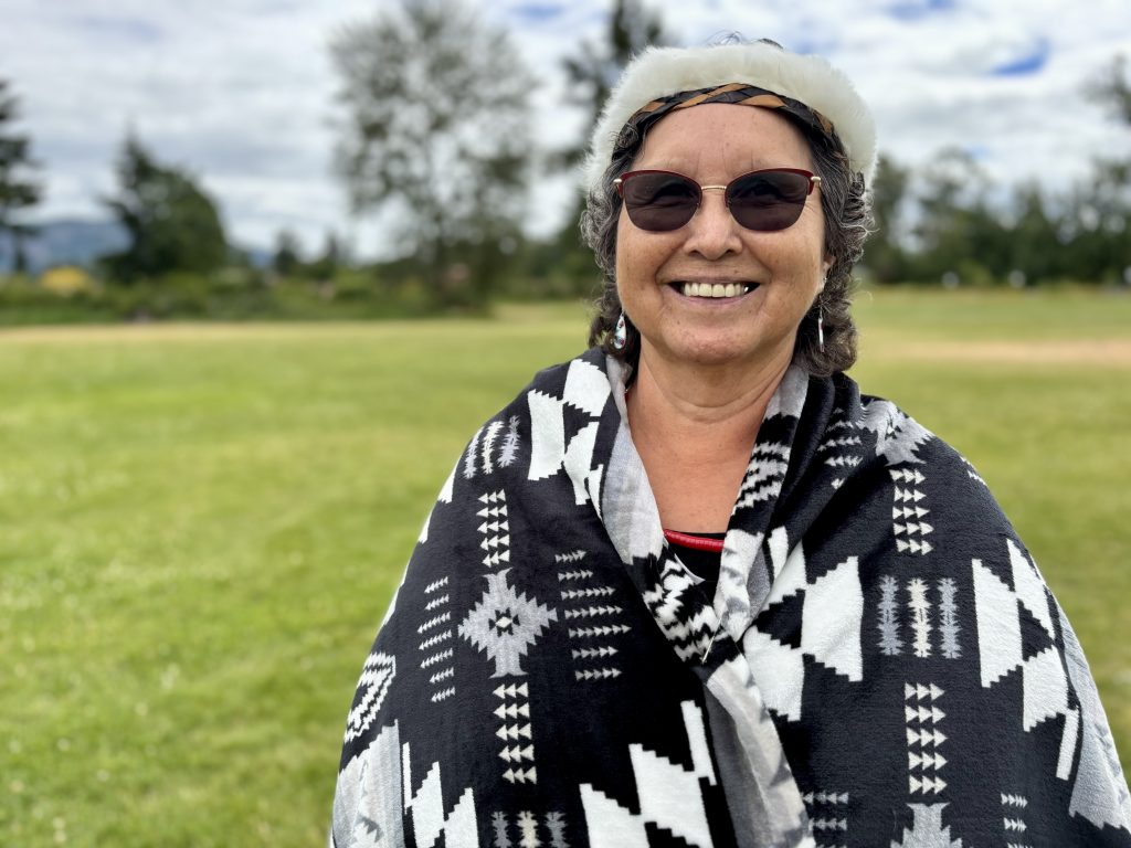 Cowichan Tribes Chief Cindy Daniels is wrapped in a traditional blanket and smiles from an open field.