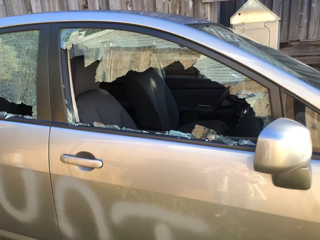 Side of a grey car with a window smashed in with spraypaint on the side. Visible letters say UNT