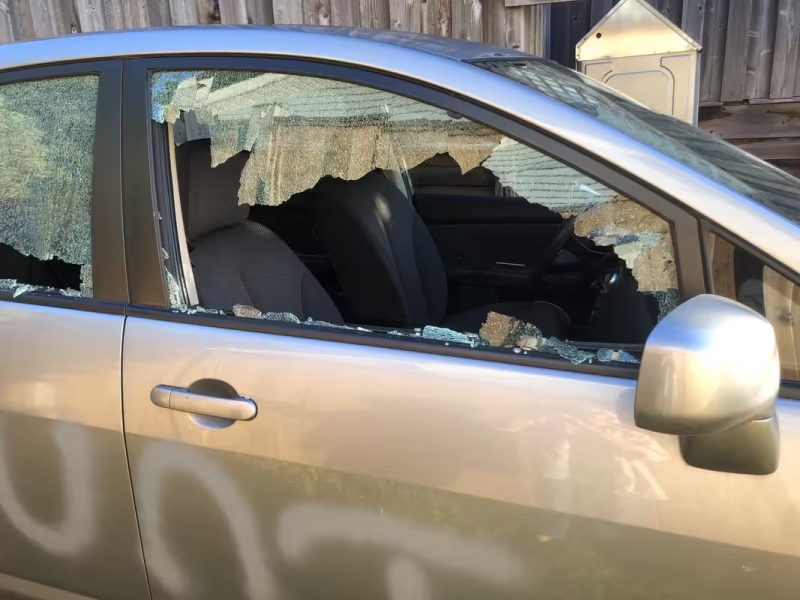 Side of a grey car with a window smashed in with spraypaint on the side. Visible letters say UNT