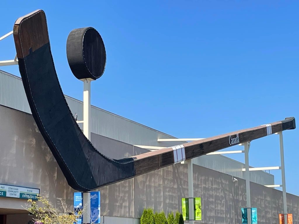 An enormous wooden hockey stick, the World's Largest Hockey Stick, bouncing a giant puck is attached to the exterior of an arena.