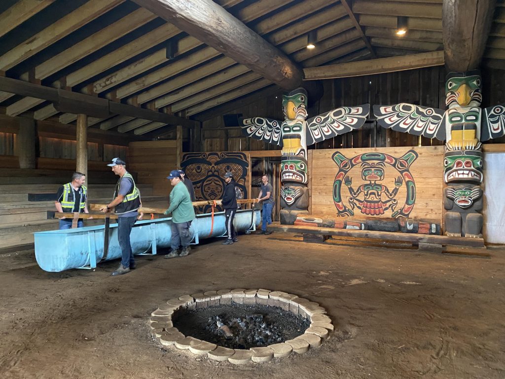 A group of people inside the K'ómoks Bighouse lifting up the fish trap to carry it out.
