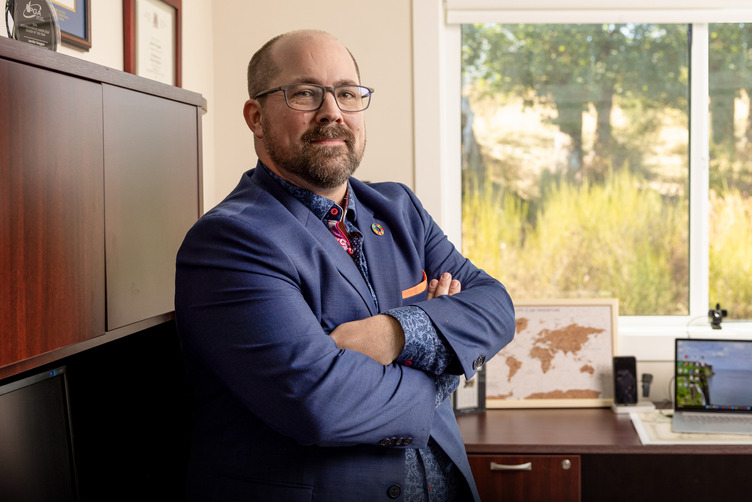 A man leans against a cubicle wall with his arms crossed, smiling at the camera. It's a headshot.