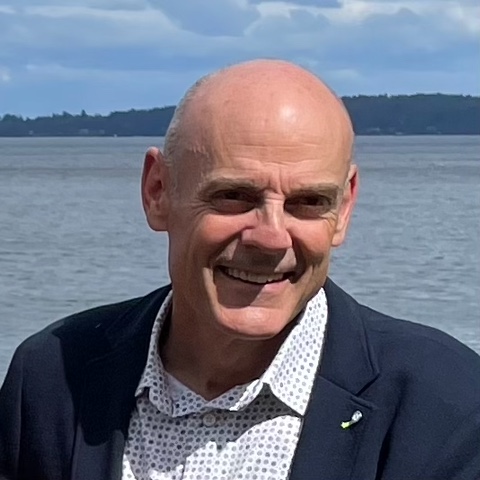 A photo of Dr. Tom Rimmer, a Cowichan family doctor. He is smiling and ocean can be seen behind him.