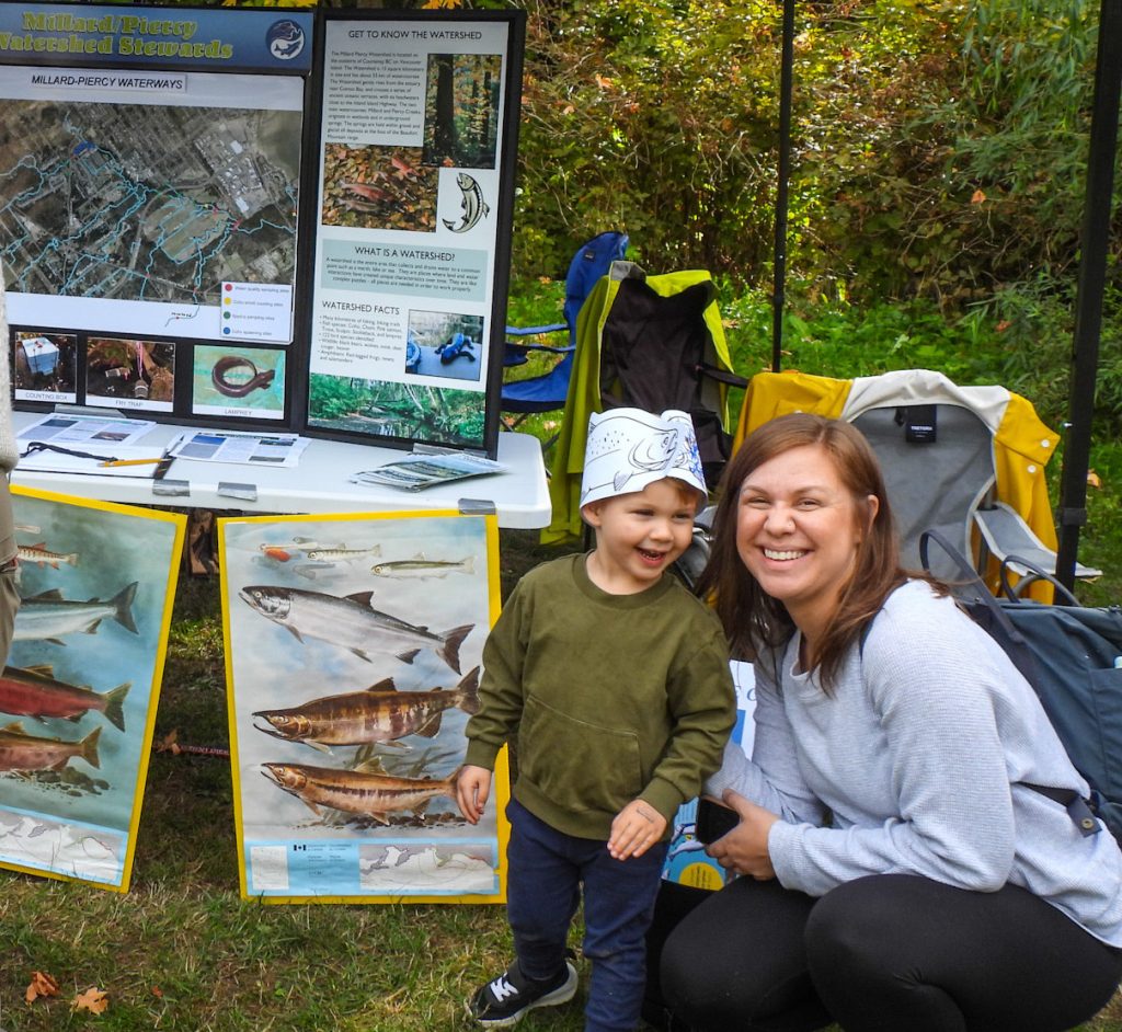 A woman and child in front of a booth with images of salmon.