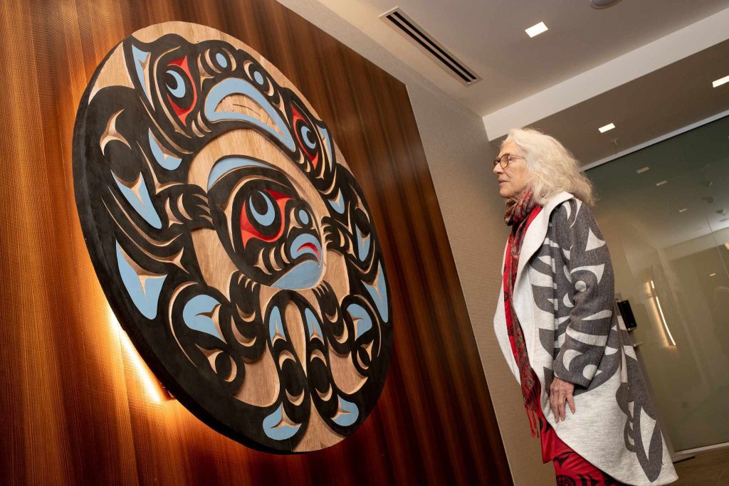 A woman looks at a large spindle whorl hanging on a wall.
